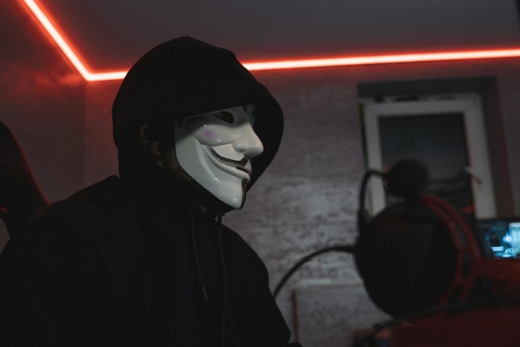 pexels-photo-5380614-5380614 Person wearing a hacker mask in a dimly lit room, symbolizing cyber security.